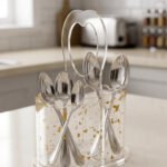 Clear acrylic spoon holder featuring decorative gold flake accents, a convenient top loop carry handle, and organized stainless steel spoons on a kitchen countertop.