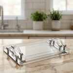 Clear acrylic serving tray set with polished handles displayed on a marble countertop in a modern kitchen setting