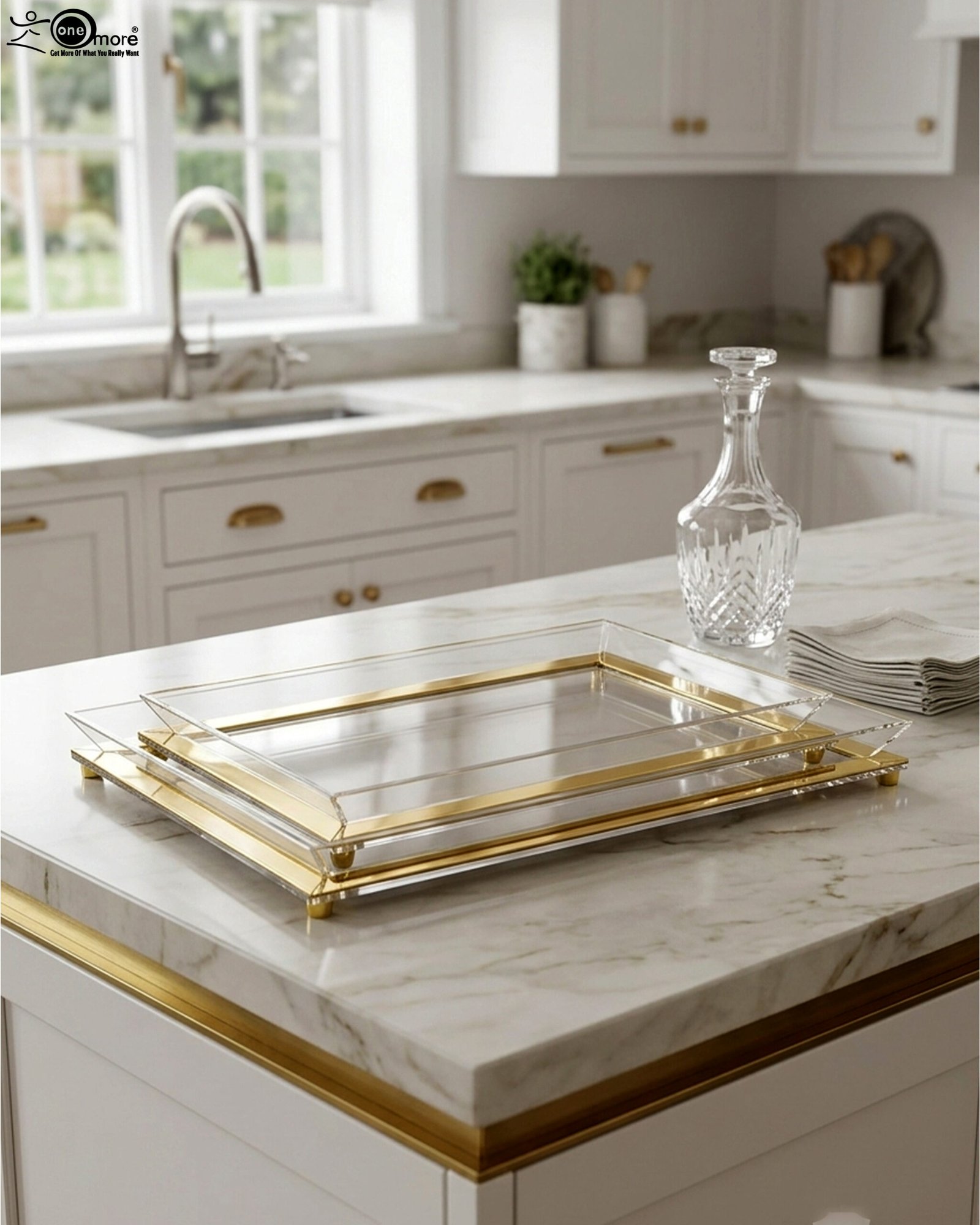 1 Two stacked luxury clear acrylic serving trays with polished gold trim and feet displayed on a white marble kitchen island.