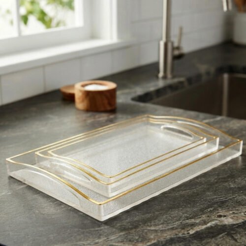 Nesting clear acrylic serving tray set with elegant gold trim and built-in handles, displayed on a modern kitchen countertop.