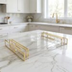 Nesting clear acrylic serving tray set with polished gold handles displayed on a white marble kitchen countertop.