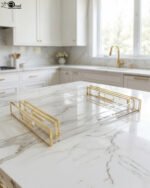 Nesting clear acrylic serving tray set with polished gold handles displayed on a white marble kitchen countertop.