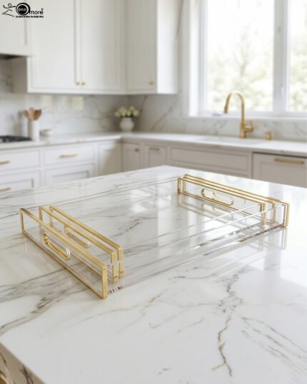 Nesting clear acrylic serving tray set with polished gold handles displayed on a white marble kitchen countertop.