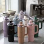A collection of 900ml insulated "Nice Time Sitarayuri Coffee" tumblers with handles displayed in various colors on a kitchen counter.