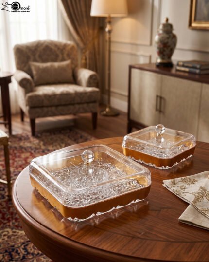 Two square crystal dry fruit dishes with gold trim bases and glass lids displayed on a wooden table in a luxury living room setting.