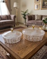Two transparent crystal dry fruit serving dishes with partitioned interiors, gold geometric patterns, and crystal-topped lids placed on a wooden table.