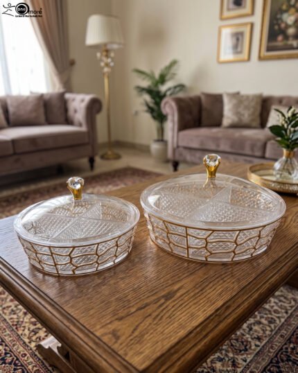 Two transparent crystal dry fruit serving dishes with partitioned interiors, gold geometric patterns, and crystal-topped lids placed on a wooden table.