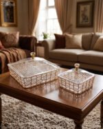 Medium and large luxury clear acrylic dry fruit dishes featuring intricate gold geometric frames and crystal-style knob lids, displayed together on a wooden coffee table in a modern living room.