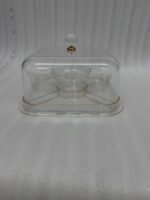 Clear acrylic cake stand with a domed lid and crystal knob displaying a frosted caramel-drizzled cake on a kitchen countertop.