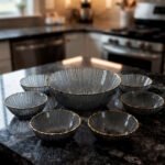Two grey ribbed glass bowls with gold trim displayed together on a modern white marble countertop