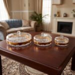 Three luxury crystal dry fruit dishes with gold rims and lids in Small, Medium, and Large sizes displayed on a dark wooden coffee table.