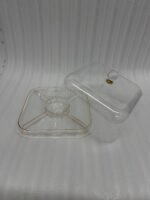 Clear acrylic cake stand with a domed lid and crystal knob displaying a frosted caramel-drizzled cake on a kitchen countertop.