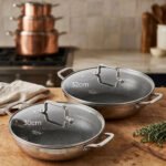 Two stainless steel honeycomb woks with glass lids and textured handles displayed on a wooden kitchen counter, featuring 30cm and 32cm sizes