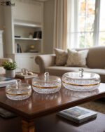 Three elegant cut-crystal dry fruit dishes with gold rims and matching spherical-handle lids displayed in Small, Medium, and Large sizes on a wooden coffee table in a modern living room.