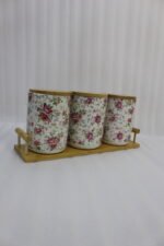 Three floral print ceramic storage jars with bamboo lids arranged on a matching wooden tray on a modern kitchen countertop