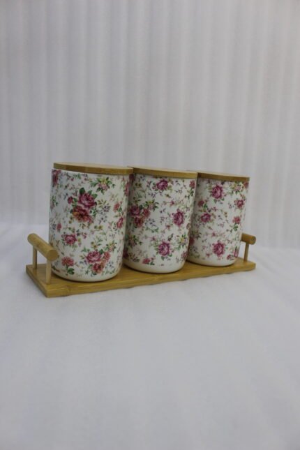 Three floral print ceramic storage jars with bamboo lids arranged on a matching wooden tray on a modern kitchen countertop