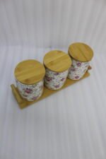 Three floral print ceramic storage jars with bamboo lids arranged on a matching wooden tray on a modern kitchen countertop