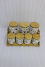 Luxury white and gold ceramic kitchen storage jar set with wooden lids arranged on a wooden display stand in a modern kitchen.