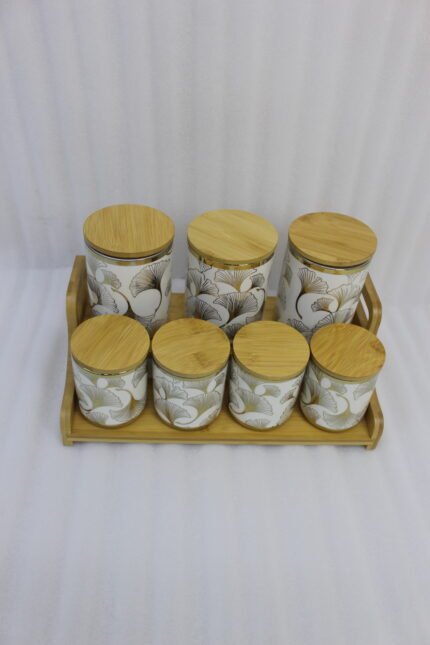 Luxury white and gold ceramic kitchen storage jar set with wooden lids arranged on a wooden display stand in a modern kitchen.