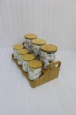 Luxury white and gold ceramic kitchen storage jar set with wooden lids arranged on a wooden display stand in a modern kitchen.