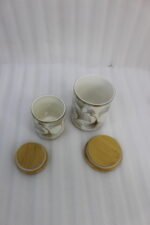 Luxury white and gold ceramic kitchen storage jar set with wooden lids arranged on a wooden display stand in a modern kitchen.