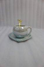 Elegant pastel ceramic cup and saucer set with a matching gold spoon and beaded handle on a marble kitchen countertop.