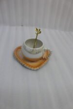 Elegant pastel ceramic cup and saucer set with a matching gold spoon and beaded handle on a marble kitchen countertop.