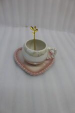 Elegant pastel ceramic cup and saucer set with a matching gold spoon and beaded handle on a marble kitchen countertop.