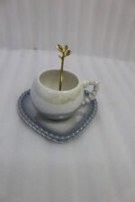 Elegant pastel ceramic cup and saucer set with a matching gold spoon and beaded handle on a marble kitchen countertop.