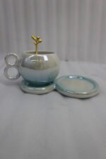 A collection of multicolored ceramic coffee cups and saucers with gold leaf spoons and double-loop handles arranged on a marble kitchen counter.