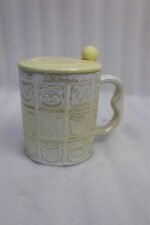 Four pastel ceramic mugs with animal embossed patterns, matching lids with round knobs, and spoons displayed on a kitchen counter