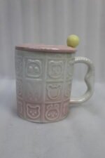 Four pastel ceramic mugs with animal embossed patterns, matching lids with round knobs, and spoons displayed on a kitchen counter