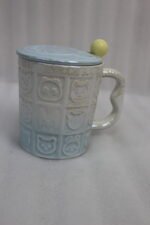 Four pastel ceramic mugs with animal embossed patterns, matching lids with round knobs, and spoons displayed on a kitchen counter