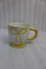 Four pastel ceramic coffee mugs with cute raised bows and matching colorful bases arranged on a marble kitchen counter.