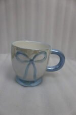 Four pastel ceramic coffee mugs with cute raised bows and matching colorful bases arranged on a marble kitchen counter.