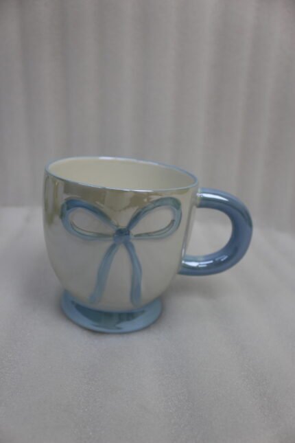 Four pastel ceramic coffee mugs with cute raised bows and matching colorful bases arranged on a marble kitchen counter.