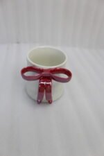 Four glossy ceramic coffee mugs with decorative bow handles in red, white, pink, and blue, arranged on a marble kitchen counter.