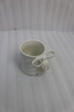 Four glossy ceramic coffee mugs with decorative bow handles in red, white, pink, and blue, arranged on a marble kitchen counter.