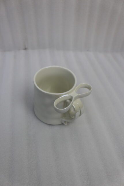 Four glossy ceramic coffee mugs with decorative bow handles in red, white, pink, and blue, arranged on a marble kitchen counter.