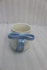 Four glossy ceramic coffee mugs with decorative bow handles in red, white, pink, and blue, arranged on a marble kitchen counter.