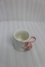 Four glossy ceramic coffee mugs with decorative bow handles in red, white, pink, and blue, arranged on a marble kitchen counter.