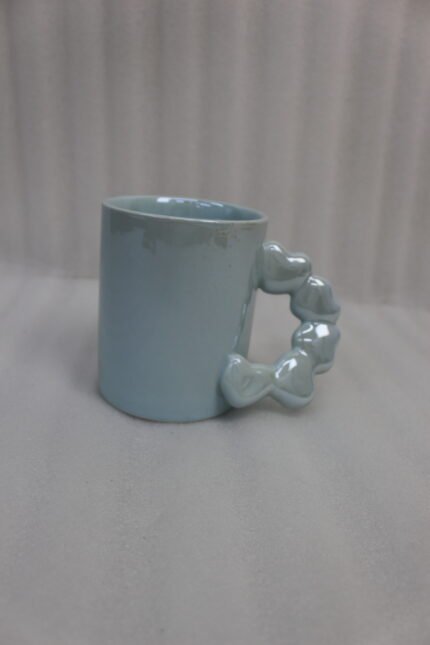 Four colorful ceramic mugs with unique bubble-textured handles arranged on a marble kitchen countertop.