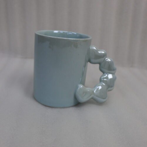 Four colorful ceramic mugs with unique bubble-textured handles arranged on a marble kitchen countertop.