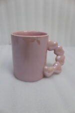 Four colorful ceramic mugs with unique bubble-textured handles arranged on a marble kitchen countertop.