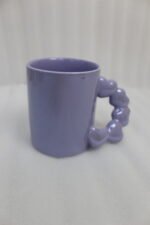 Four colorful ceramic mugs with unique bubble-textured handles arranged on a marble kitchen countertop.