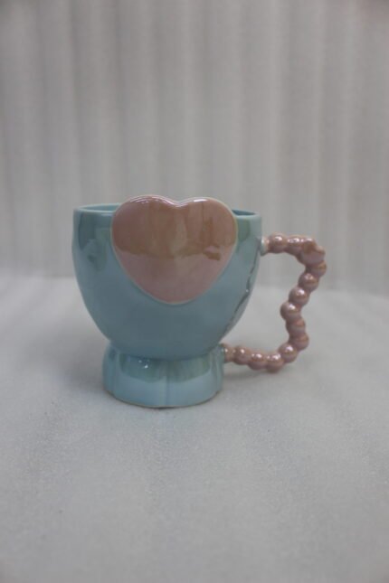 Four colorful ceramic mugs featuring heart accents and beaded handles lined up on a kitchen counter.