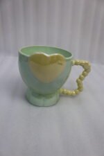Four colorful ceramic mugs featuring heart accents and beaded handles lined up on a kitchen counter.