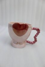 Four colorful ceramic mugs featuring heart accents and beaded handles lined up on a kitchen counter.