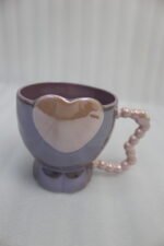 Four colorful ceramic mugs featuring heart accents and beaded handles lined up on a kitchen counter.