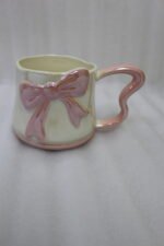 Four pastel ceramic coffee mugs with cute 3D bows and heart-shaped handles lined up on a kitchen counter.